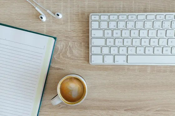 Bureau vu de dessus : carnet ouvert, tasse de café et clavier